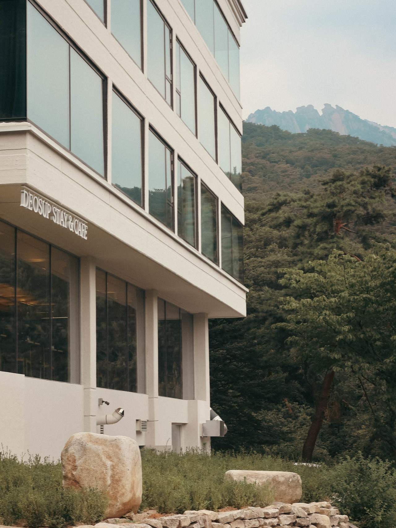 북한산 능선을 배경으로 한 본관 외벽과 DEOSUP STAY & CAFE 사인