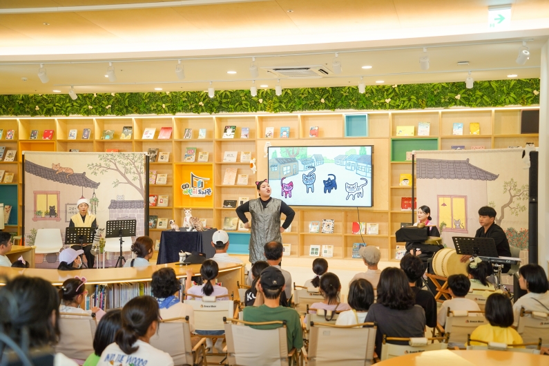 곡성어린이도서관 로비의 동화책이 진열된 책장을 배경으로 캠핑의자에 앉은 관객들이 나는고양이로소이다 공연을 관람하는 모습
