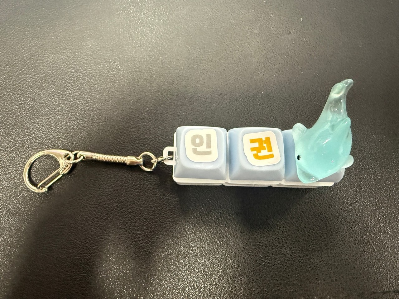 열쇠고리가 달린 작은 받침에 키캡 세 개가 끼워져 있고, ‘인’·‘권’ 글자와 하늘색 고래 모양 장식이 함께 붙어 있는 모습