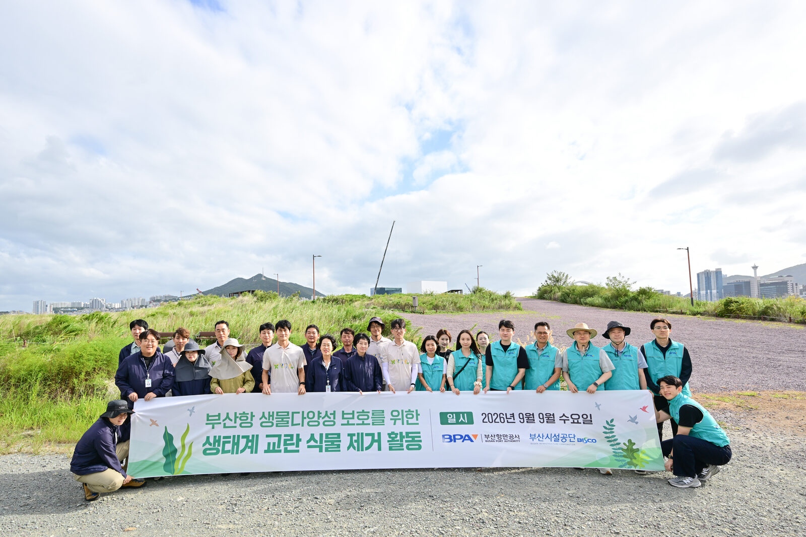 조끼를 맞춰 입은 BPA·부산시설공단 임직원이 북항 친수공원에서 생태계 교란 식물 제거 활동 현수막을 앞세워 단체 촬영한 모습