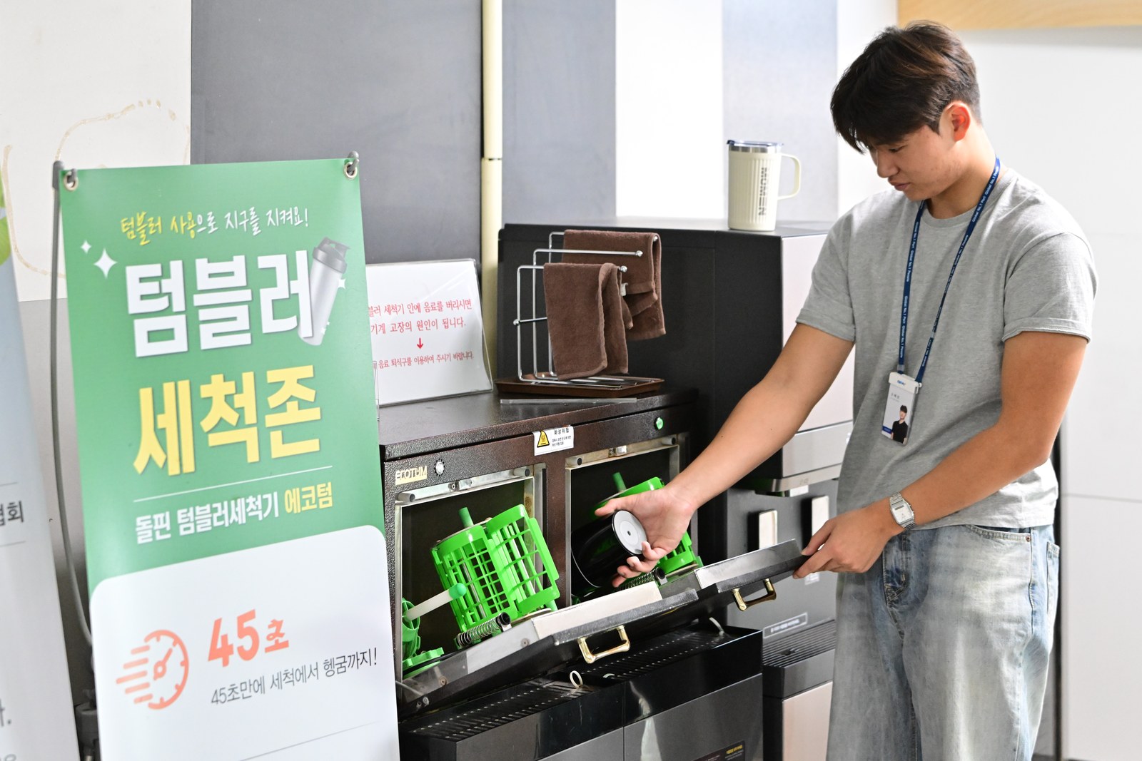 사내 텀블러 세척존에서 직원이 텀블러를 세척기에 넣는 모습. 45초 세척을 안내하는 입간판이 함께 보인다