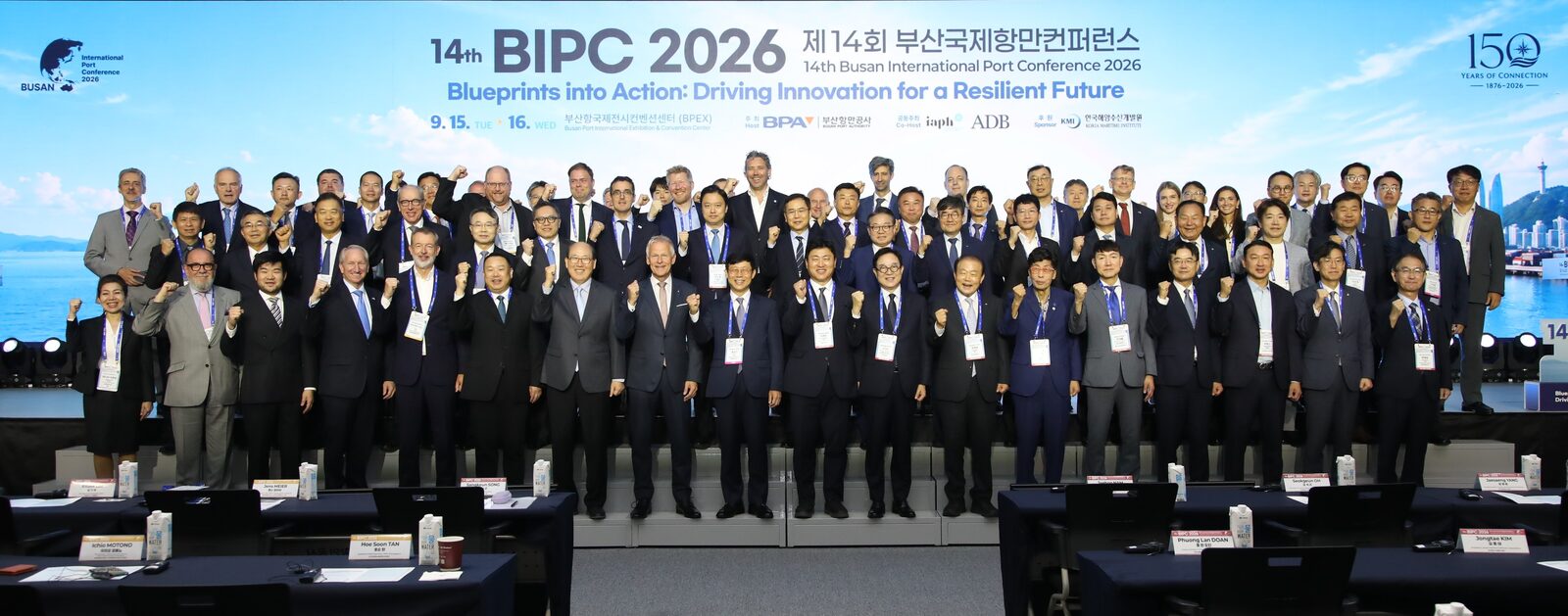 '14th BIPC 2026 제14회 부산국제항만컨퍼런스' 대형 화면 앞 무대에 수십 명의 참석자가 줄지어 서서 기념 촬영을 하는 모습. 화면에 9.15.~16. 일정과 150주년 로고가 보인다