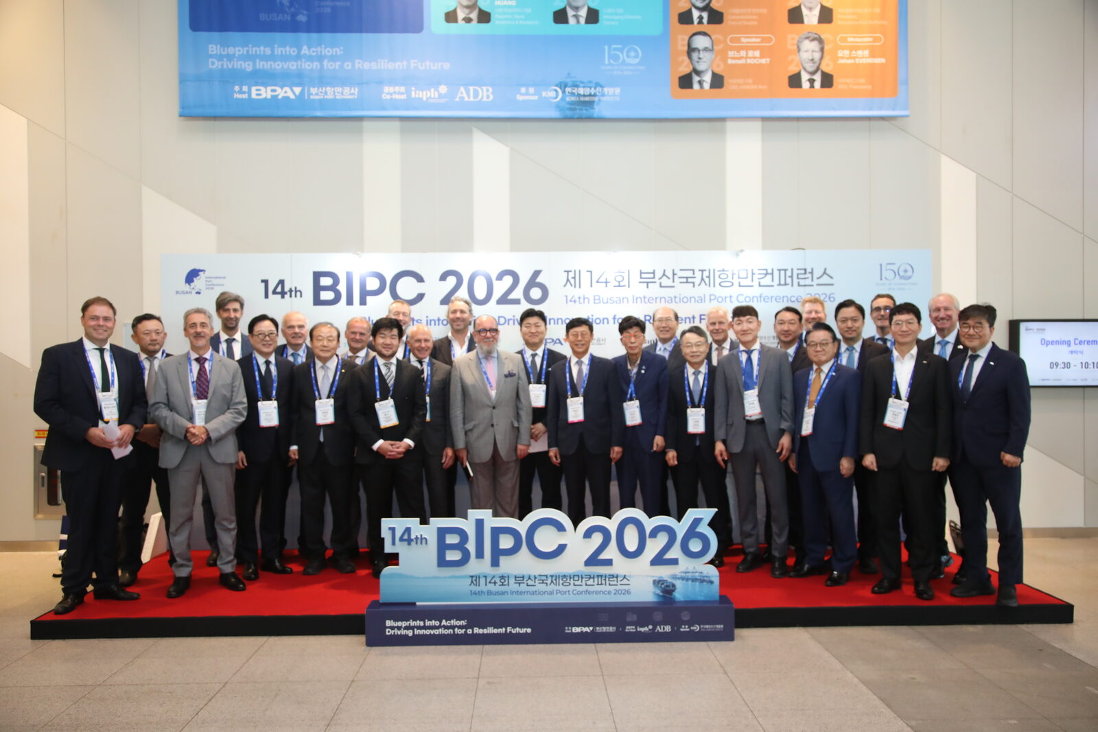 BIPC 2026 조형물이 놓인 무대 위에서 참석자들이 두 줄로 서서 기념 촬영을 하는 모습. 뒤 화면에 'Blueprints into Action: Driving Innovation for a Resilient Future'가 적혀 있다