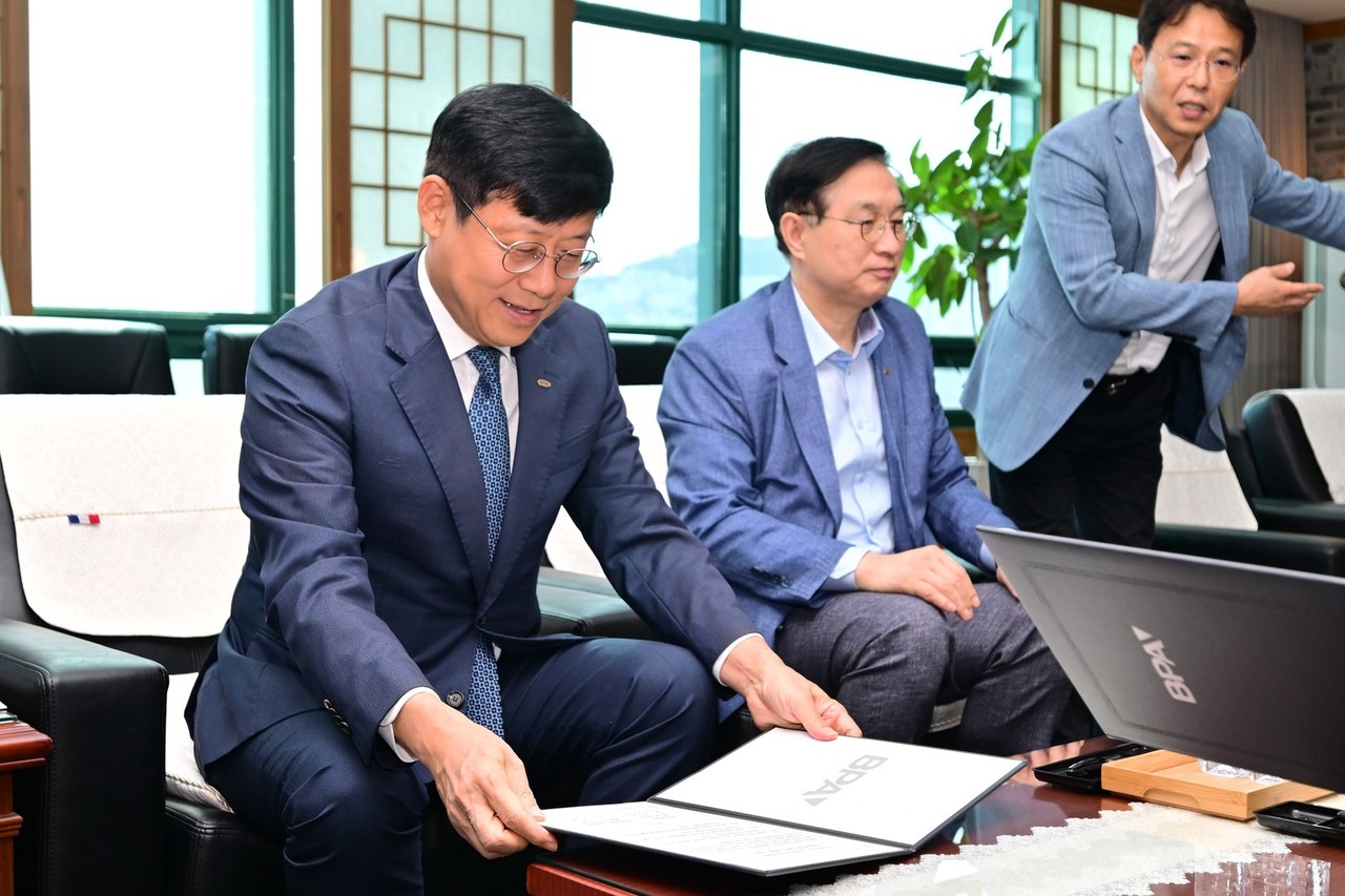 정장을 입은 두 사람이 나란히 앉아 책상 위 선언문에 서명하는 모습