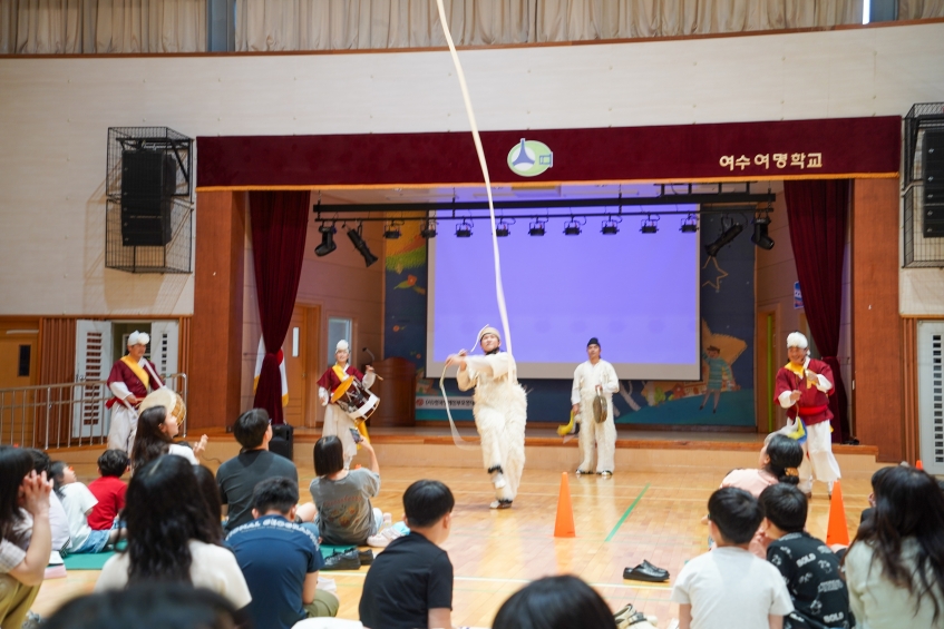**알트태그:**   천장 높이 펼쳐진 상모끈의 궤적을 따라 바라보는 여수여명학교 관객과 열두발 상모놀이