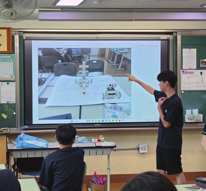 교실 큰 화면 앞에서 로봇 실습 결과를 발표하는 학생