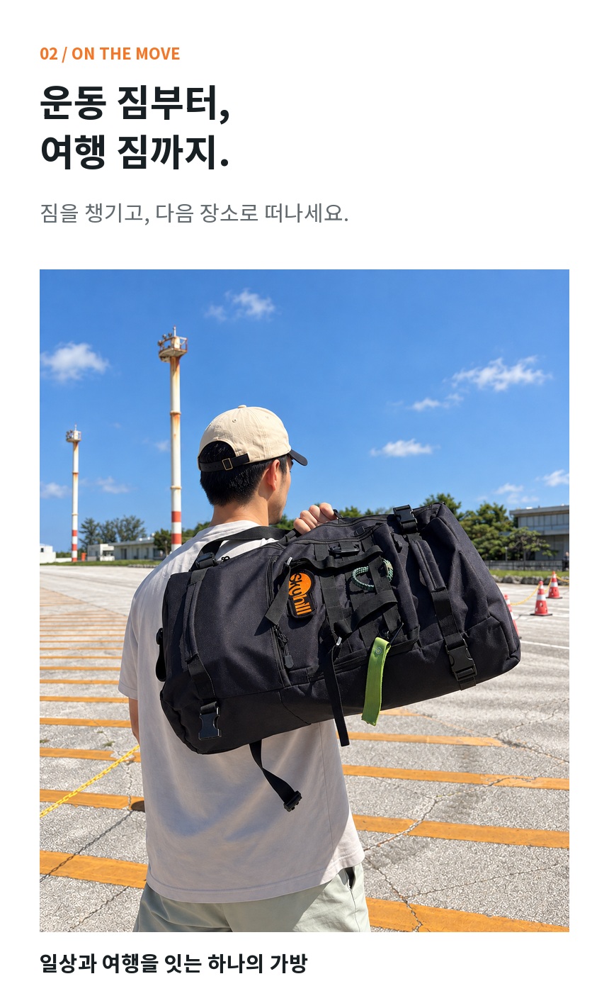 야외 여행 공간에서 후크건 손잡이를 잡아 어깨에 들어 올린 남성 모델의 착용 이미지. 포켓과 웨빙, 버클을 보여주는 각도.