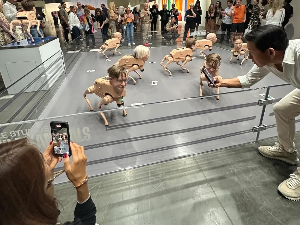 People looking at phones, looking at rBeeple's humanoid pig-dogs at Art Basel Miami Beach Daniel Cassady