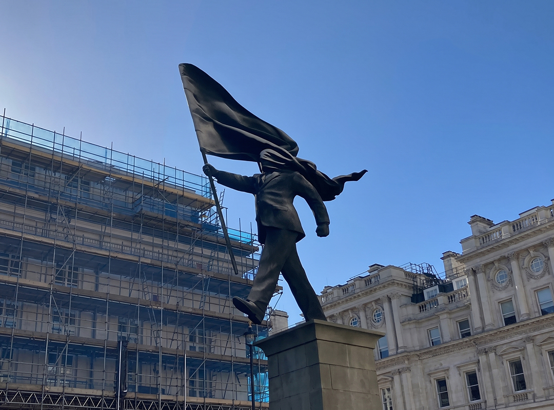 Ledt view of Banksy statue erected Waterce, St James, London 30 April 2026 - figure with face covered by flag striding off end of plinth. MumphingSquirrel - Own work