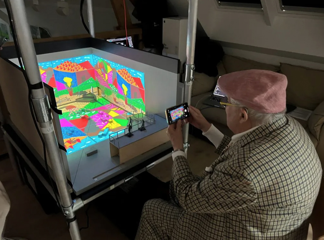 David Hockney viewing a scale model for “Bigger & Closer” created by 59 Productions. Seen on the walls are a projection of August 2021, Landscape with Shadows. Photo courtesy of Mark Grimmer.