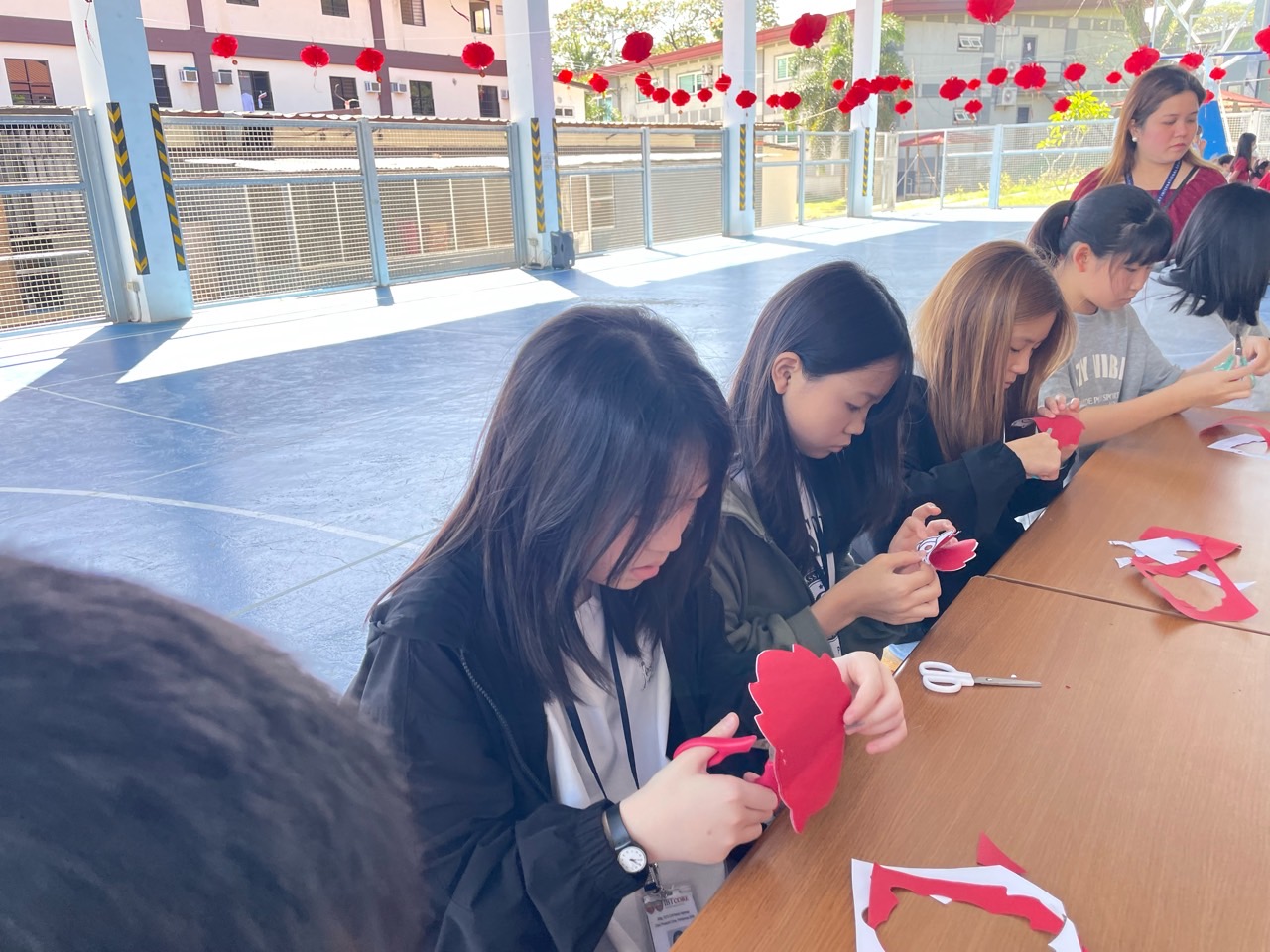 긴 테이블에 둘러앉아 붉은 종이를 오리고 꾸미는 학생들