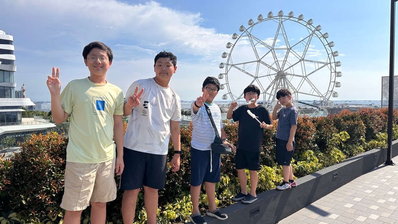 관람차와 푸른 하늘을 배경으로 기념사진을 찍는 학생들