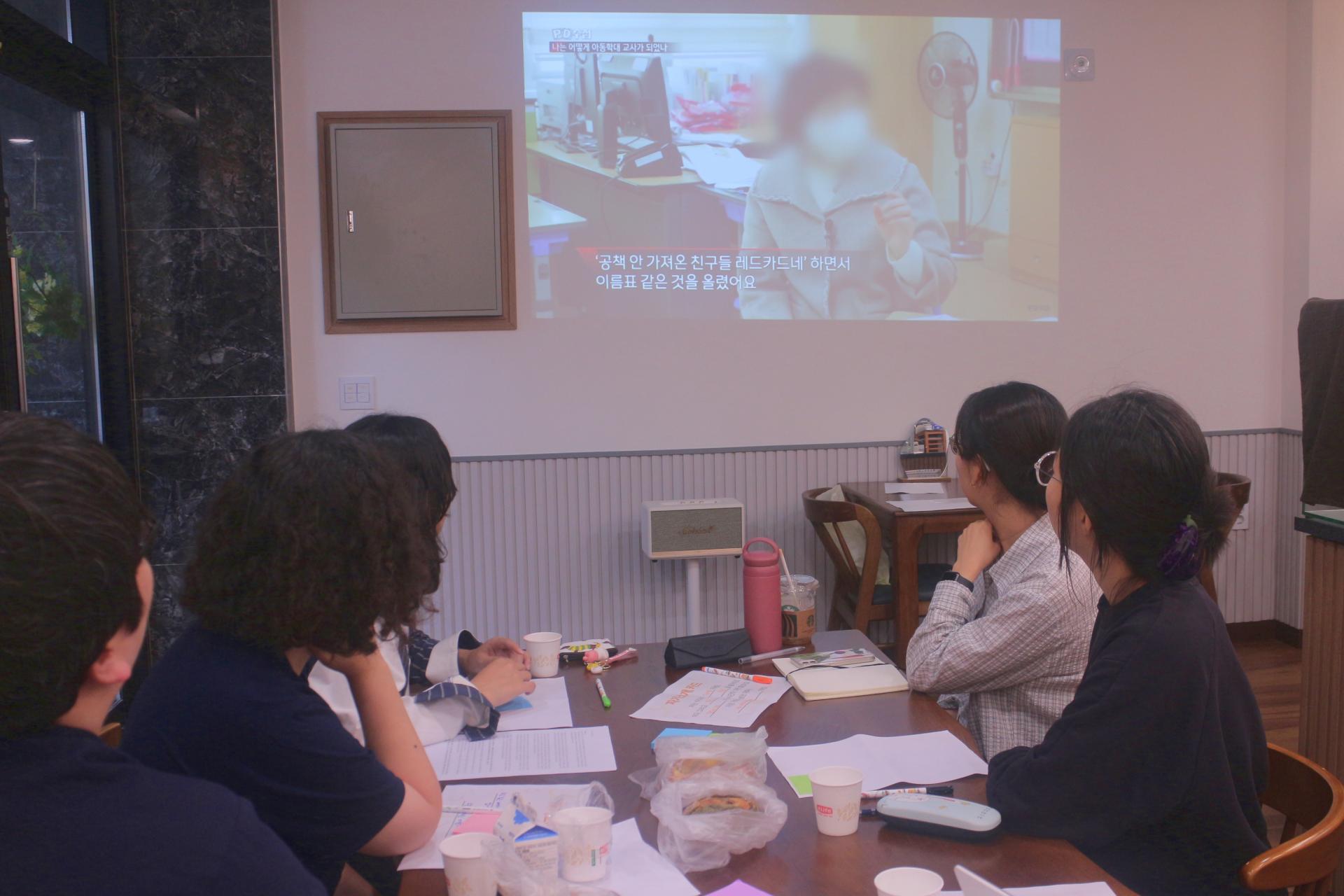 참여자들이 책상에 앉아 빔 프로젝터로 영상을 시청하고 있다. 