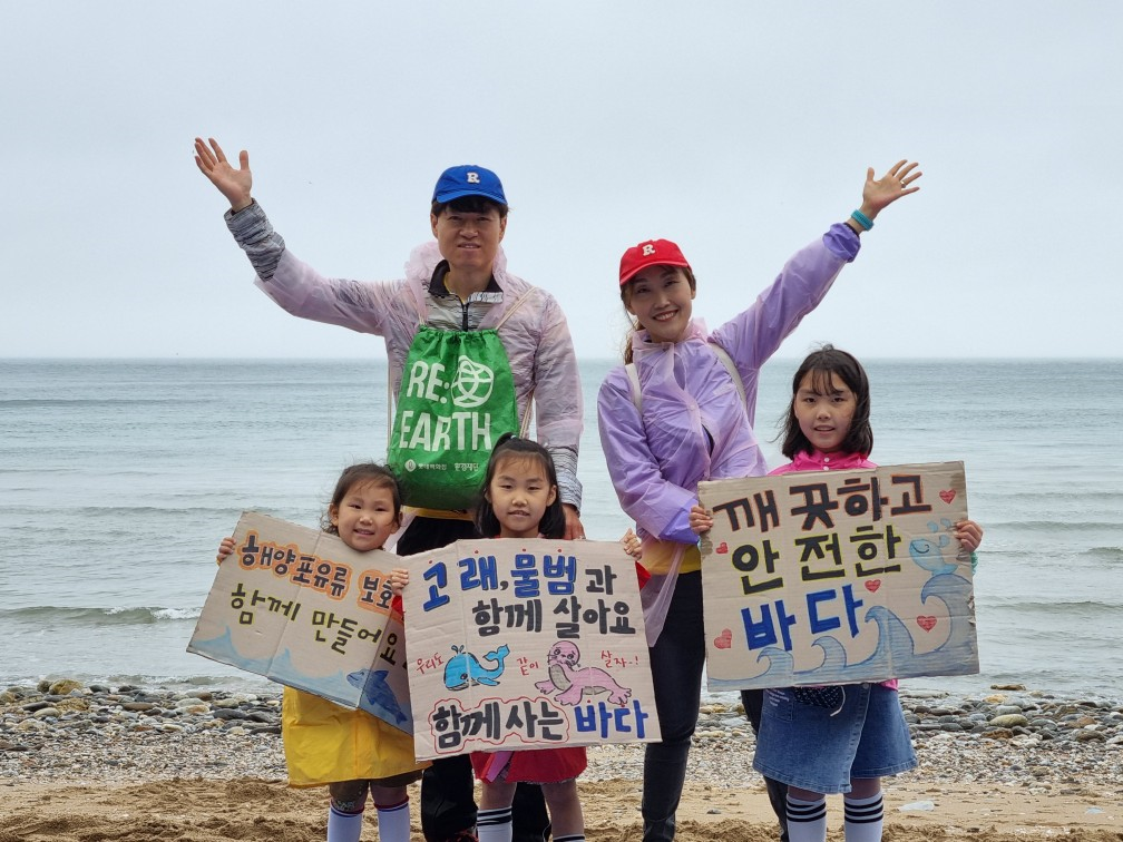 바다를 배경으로 세 어린이와 두 어른이 해양 보호를 독려하는 문구가 쓰인 피켓을 들고 포즈를 취하고 있다.