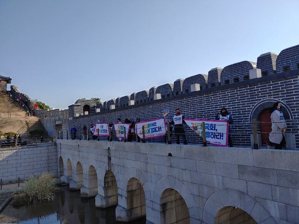 화성행궁 안에 성벽 앞에서 차별금지법 제정을 촉구하는 피켓을 들고 있는 다수의 사람들이 일열로 서있다.