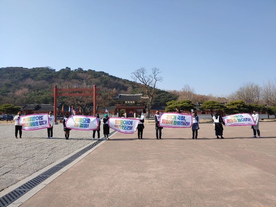 화성행궁 앞에서 다양한 피켓을 든 다수의 사람들이 일열로 서있다.