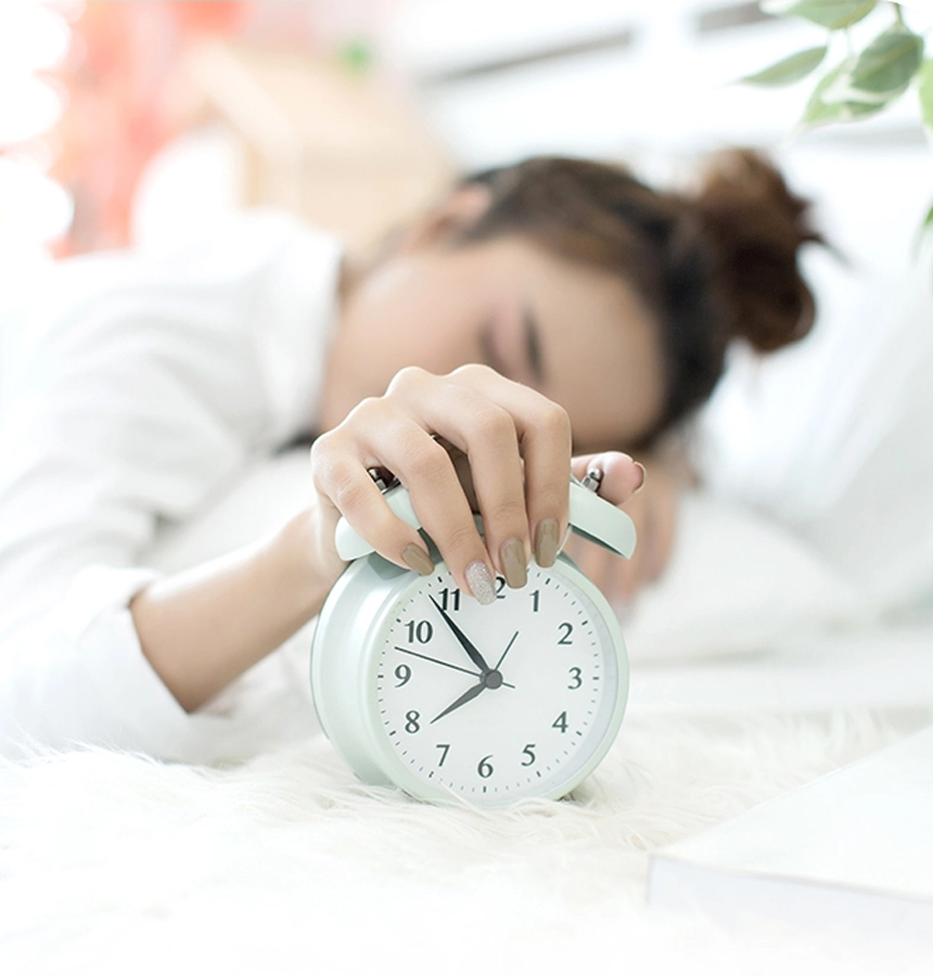 Person resting in bed while holding an alarm clock, symbolizing interrupted or insufficient sleep