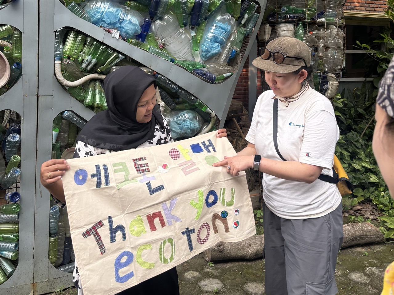 폐플라스틱 조형물 앞에서 ‘에코톤·알맹 Thank you ecoton’이라고 쓰인 현수막을 들고 있다.