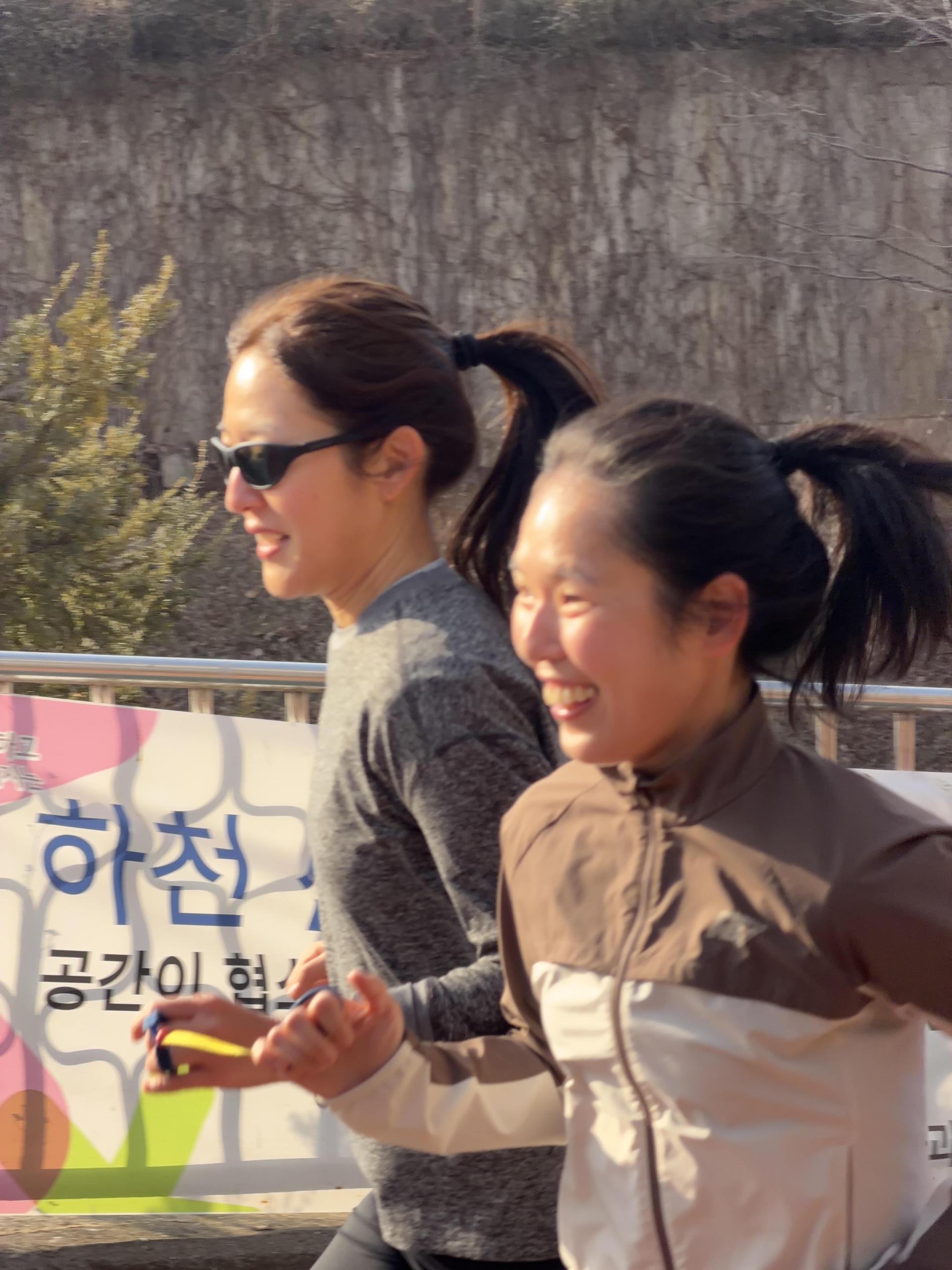 시각장애인 러너와 비장애인 가이드러너가 서로의 손을 가이드 끈으로 연결한 채 나란히 발을 맞춰 달리고 있는 모습입니다.