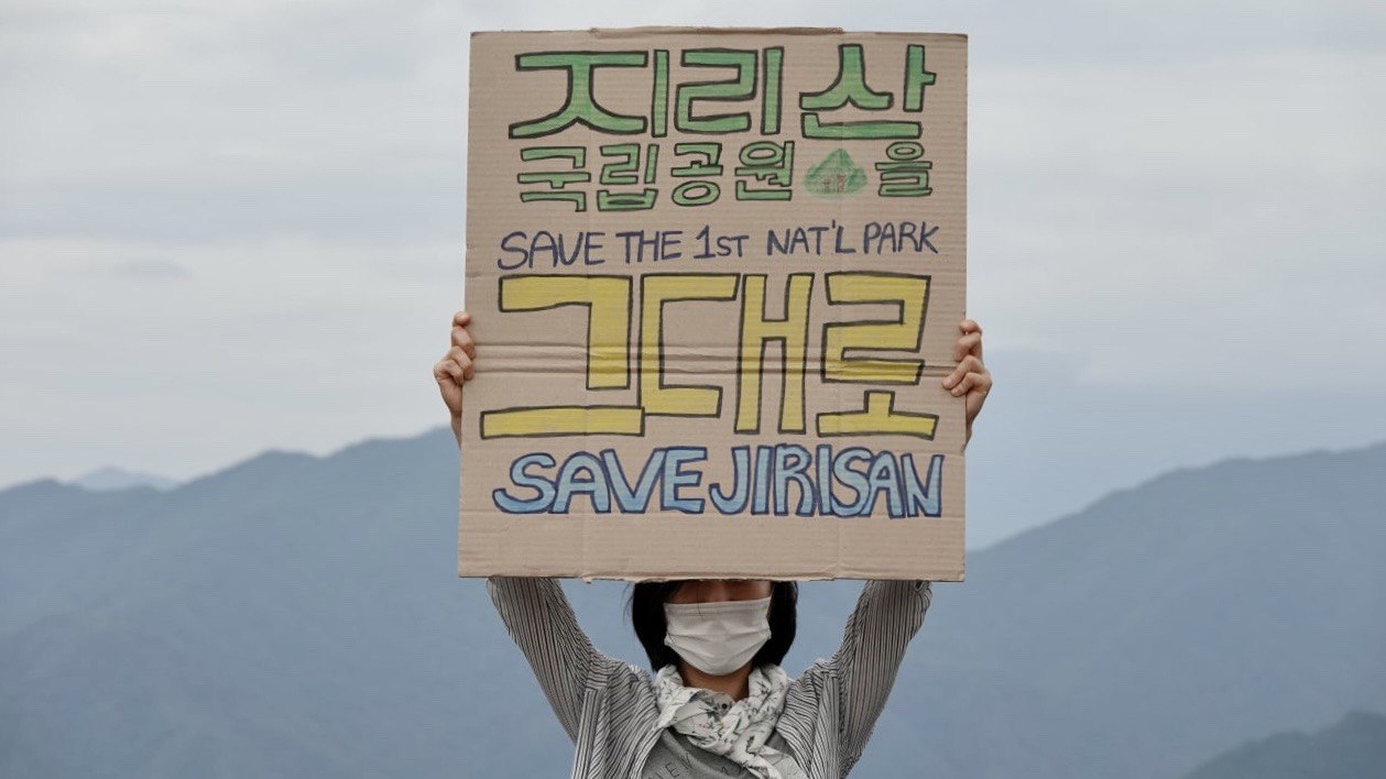 지리산국립공원의 산맥들이 뒤로 멀리 보이며, '지리산 국립공원을 그대로' 피켓을 머리 위로 들고 있는 사람이 있다.
