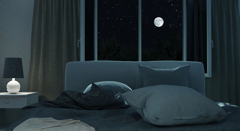 조명이 켜진 어두운 방에 있는 침대와 창 밖으로 보이는 달