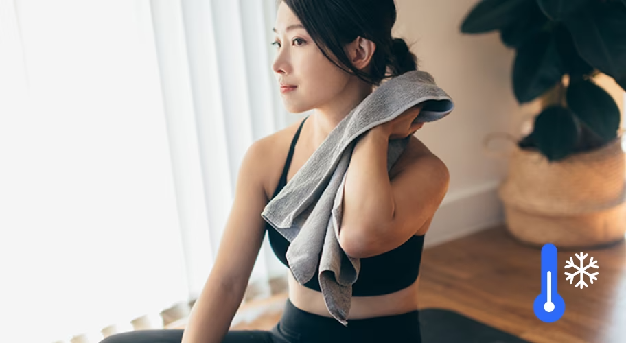 운동복 차림으로 매트에 앉아 수건으로 땀을 닦고 있는 여자와 냉방 아이콘