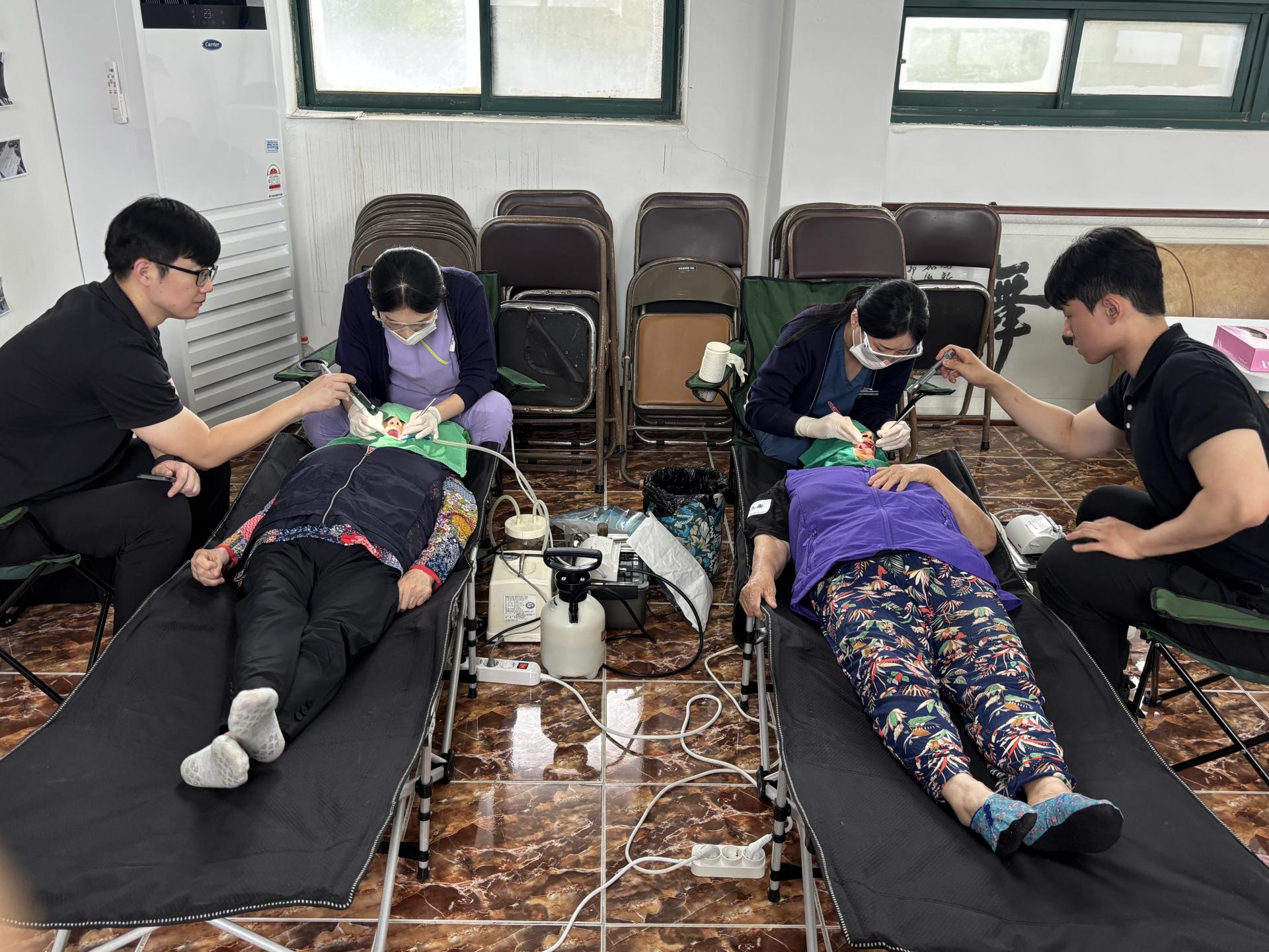 이가리마을회관에서 진행된 의료봉사 현장. 간호사와 의료진이 간이 진료 침대에 누운 어르신들의 구강 건강을 체크하고 치료를 하고 있다. 어르신들은 편안히 누워 있으며, 의료진은 정밀하게 구강 상태를 살피며 치료를 진행 중이다.