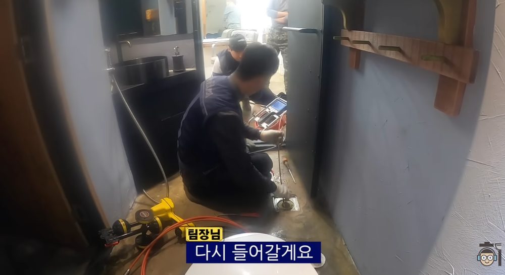 작업자가 바닥 배수구에 전문 장비를 넣어 배관을 점검하는 모습