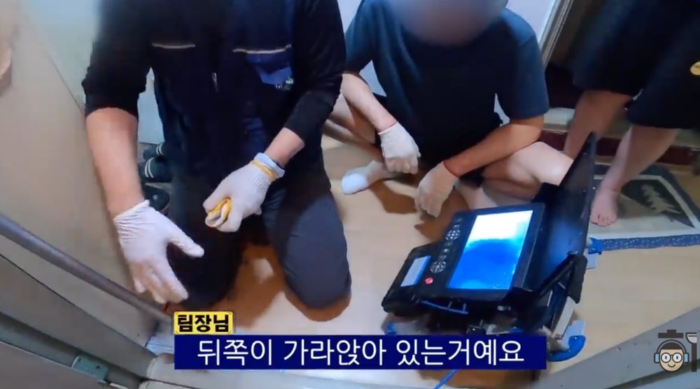작업자가 고객 앞에서 배관이 뒤쪽으로 가라앉은 구조와 막힘 원인을 설명하는 장면