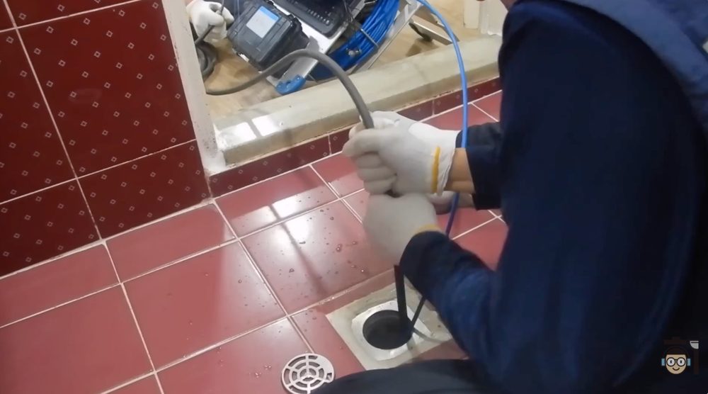 작업자가 바닥 배수구에 샤프트 장비를 넣어 배관 내부의 기름 찌꺼기를 제거하는 장면