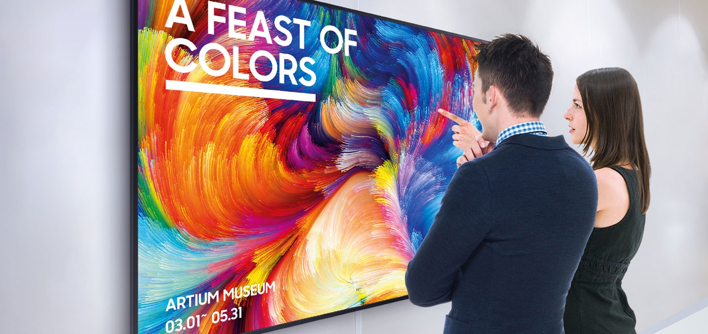 사이니지 단독형 UHD M 시리즈가 벽에 걸려있으며, 한 남성과 여성이 이야기를 나누고 있습니다.