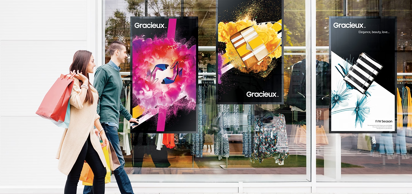 두 남녀가 걸어가고 있습니다. 왼쪽 벽면에 스마트 사이니지 실외용이 보이고 있습니다.