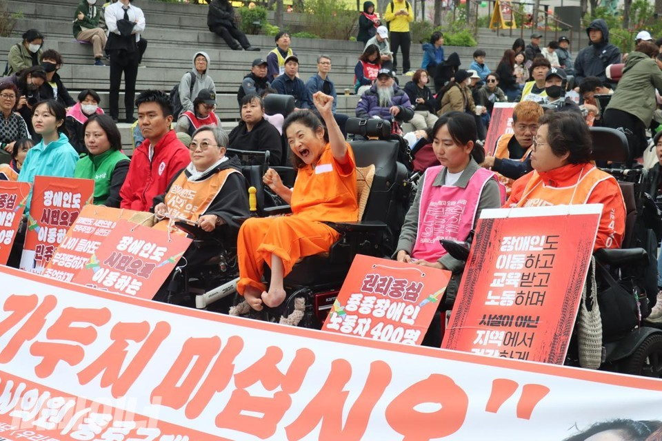 조상지 서울시의원 종로 제2선거구 예비후보가 20일 서울 광화문 해치마당에서 출마 선언 기자회견을 진행하고 있다. 진보정당 대표, 장애인 단체 활동가들 가운데, 주황색의 수용인복을 입은 조상지 후보가 한쪽 손을 들어 구호를 외치고 있다. 사진 이재민