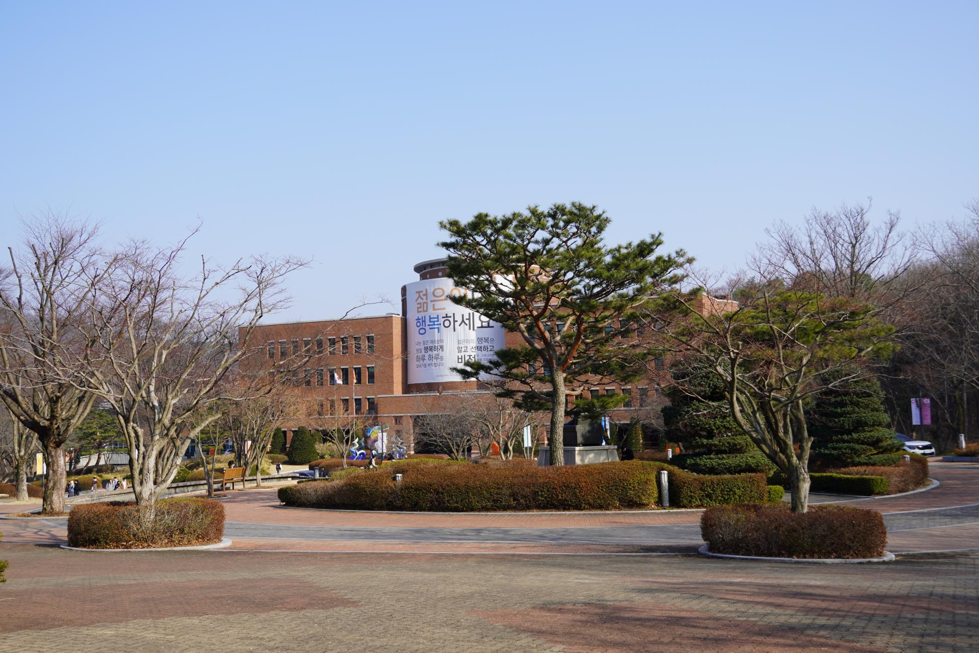 대학 캠퍼스에 붉은 벽돌빛 건물이 서있고 몇 그루의 나무들 위로 하늘이 보인다.