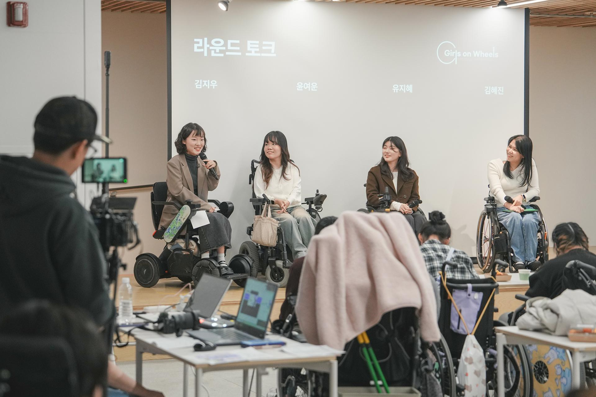 사회자와 세 명의 연사가 무대 위에 나란히 앉아있는 모습. 모두 휠체어에 앉아있고 밝게 웃고있다.