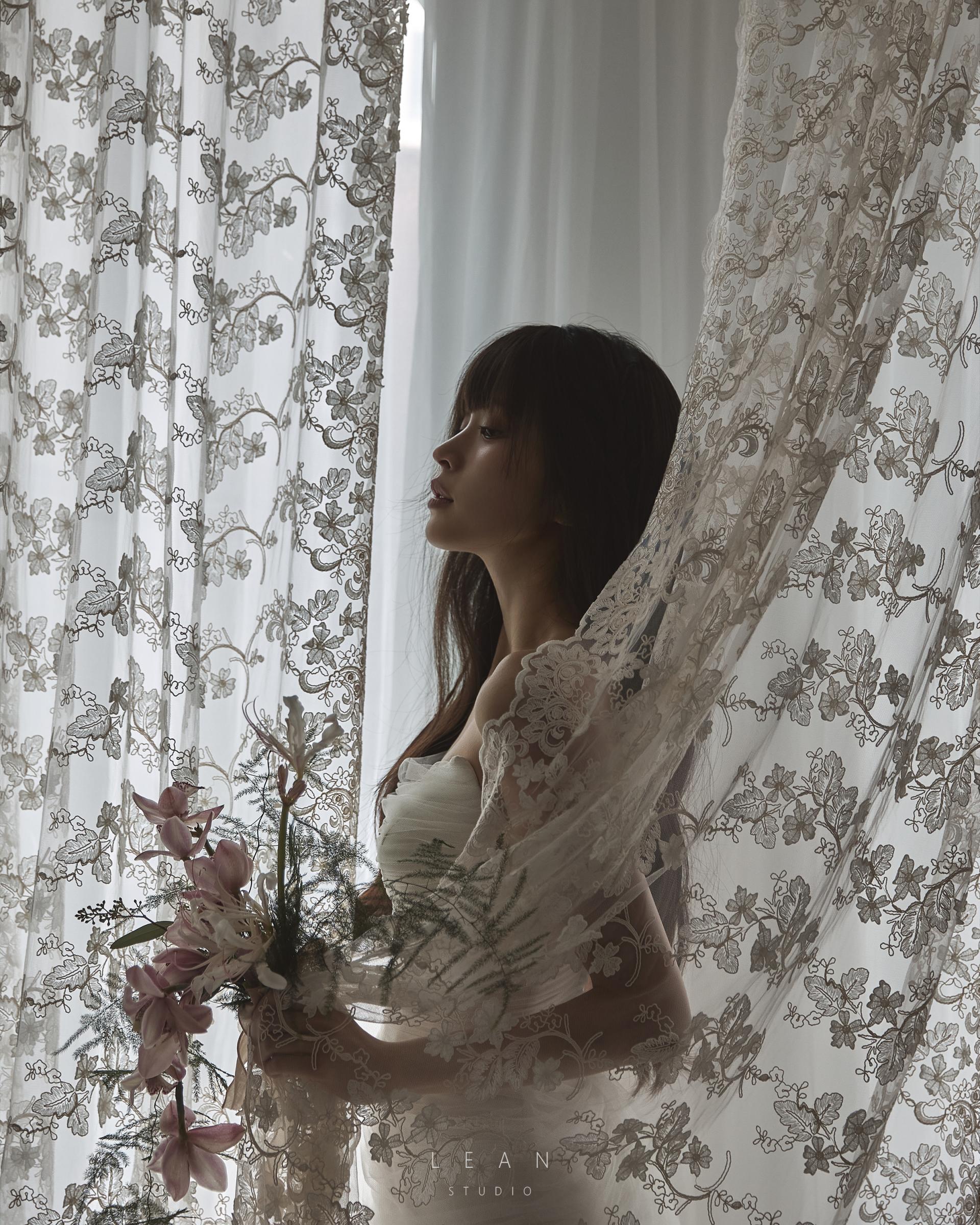 르안스튜디오 웨딩 스튜디오 자연광이 스며드는 창가의 플라워 레이스 커튼 사이에서 핑크 오키드 부케를 든 신부의 감성적인 단독 웨딩 촬영컷