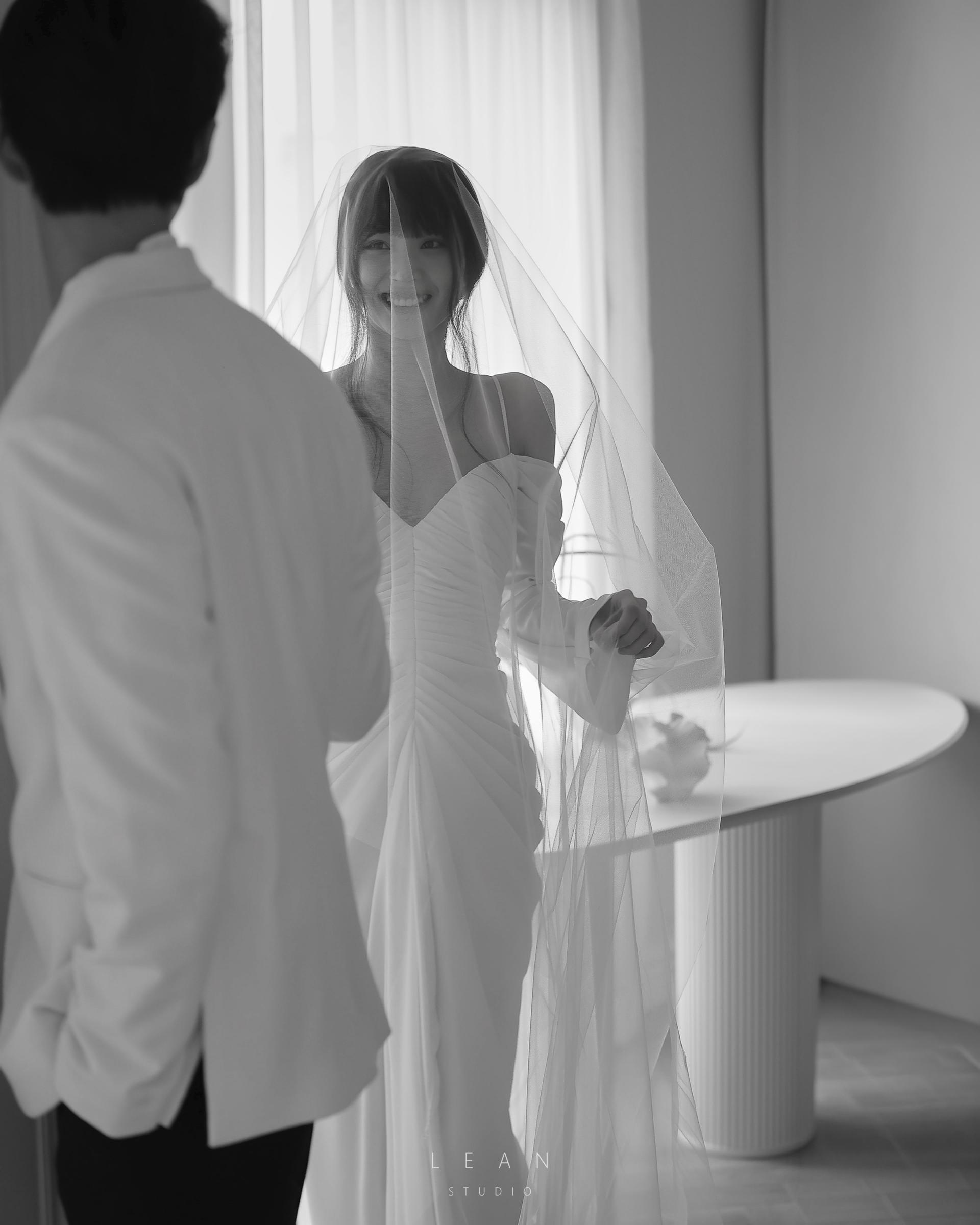 르안스튜디오 웨딩 스튜디오 롱 베일을 쓴 신부가 화이트 재킷을 입은 신랑을 바라보며 환하게 미소 짓는 자연광 흑백 웨딩 촬영컷