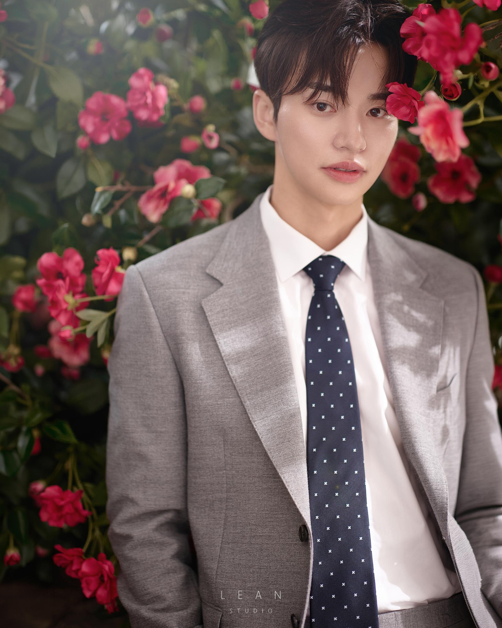 르안스튜디오 웨딩 스튜디오 붉은 꽃과 짙은 녹음을 배경으로 그레이 수트와 네이비 타이를 착용한 신랑의 플라워씬 인물 클로즈업 웨딩 촬영컷