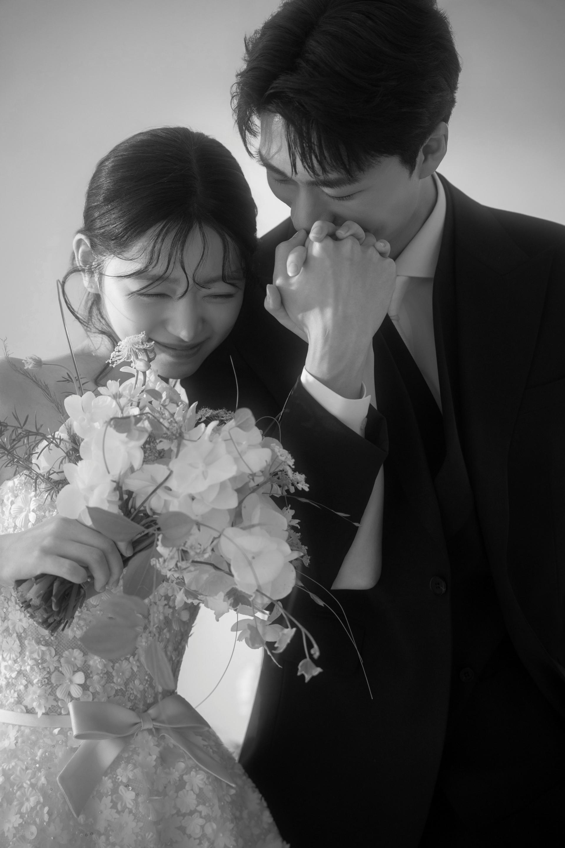 로렌하우스 웨딩 스튜디오 화이트 부케를 든 신부의 손등에 신랑이 입을 맞추는 모습을 흑백 감성으로 담은 커플 웨딩 사진