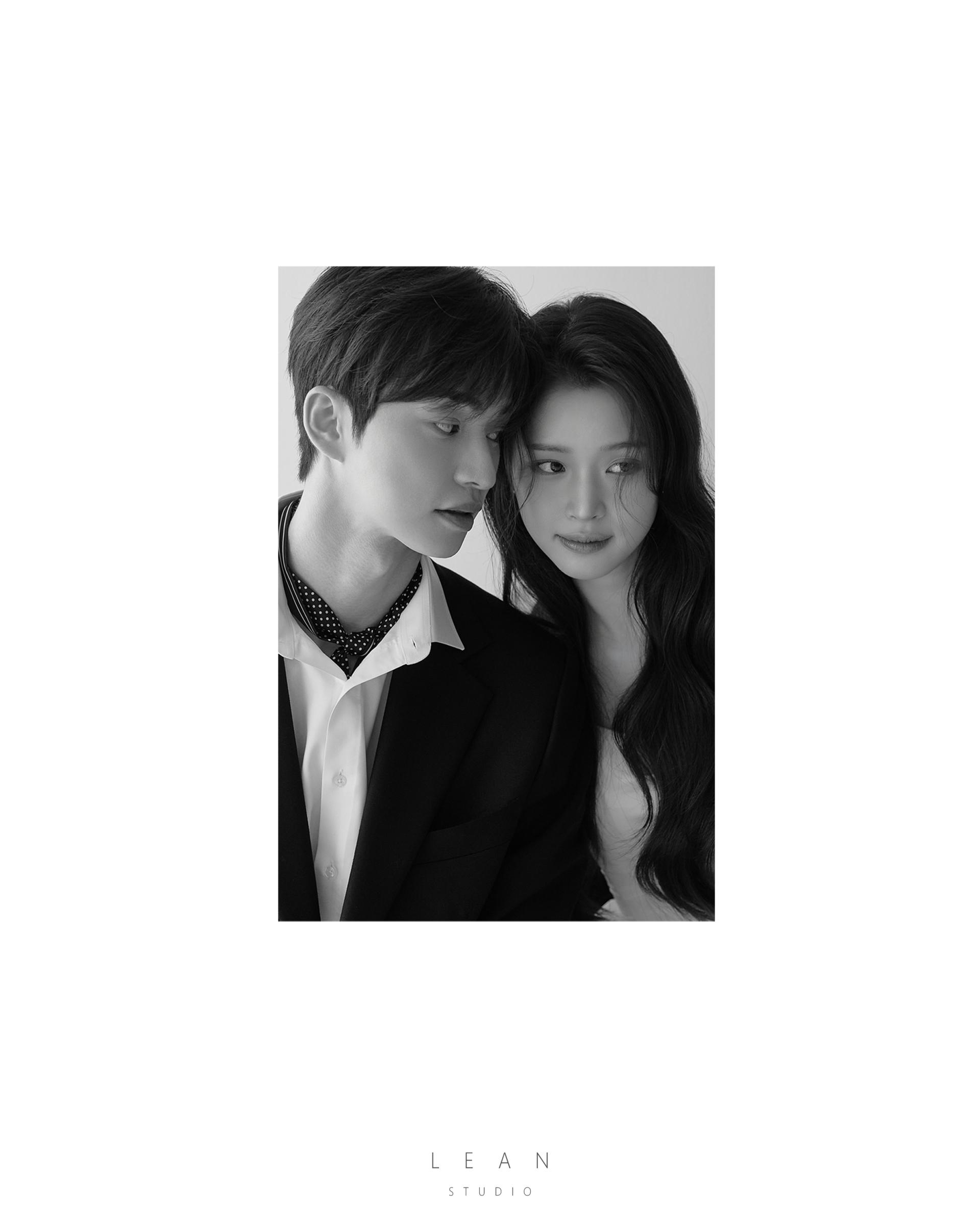 르안 웨딩 스튜디오 블랙 수트를 입은 신랑과 신부가 얼굴을 가까이 맞댄 모습을 여백 있는 세로 프레임으로 담아낸 흑백 클로즈업 웨딩 촬영컷