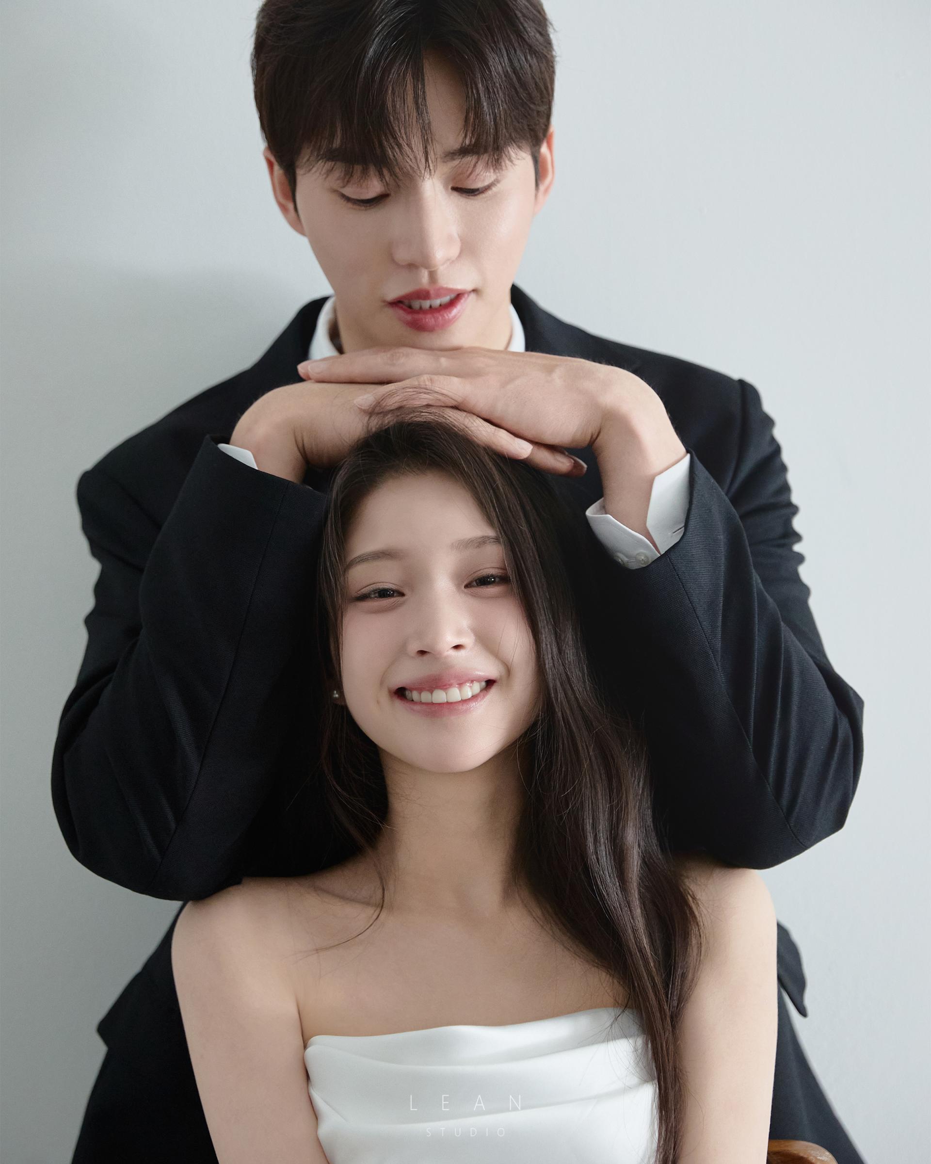 르안 웨딩 스튜디오 블랙 수트를 입은 신랑이 화이트 웨딩드레스를 입은 신부의 머리 위로 두 손을 포개고 함께 미소 짓는 모습을 가까이 담은 자연스러운 커플 웨딩 사진
