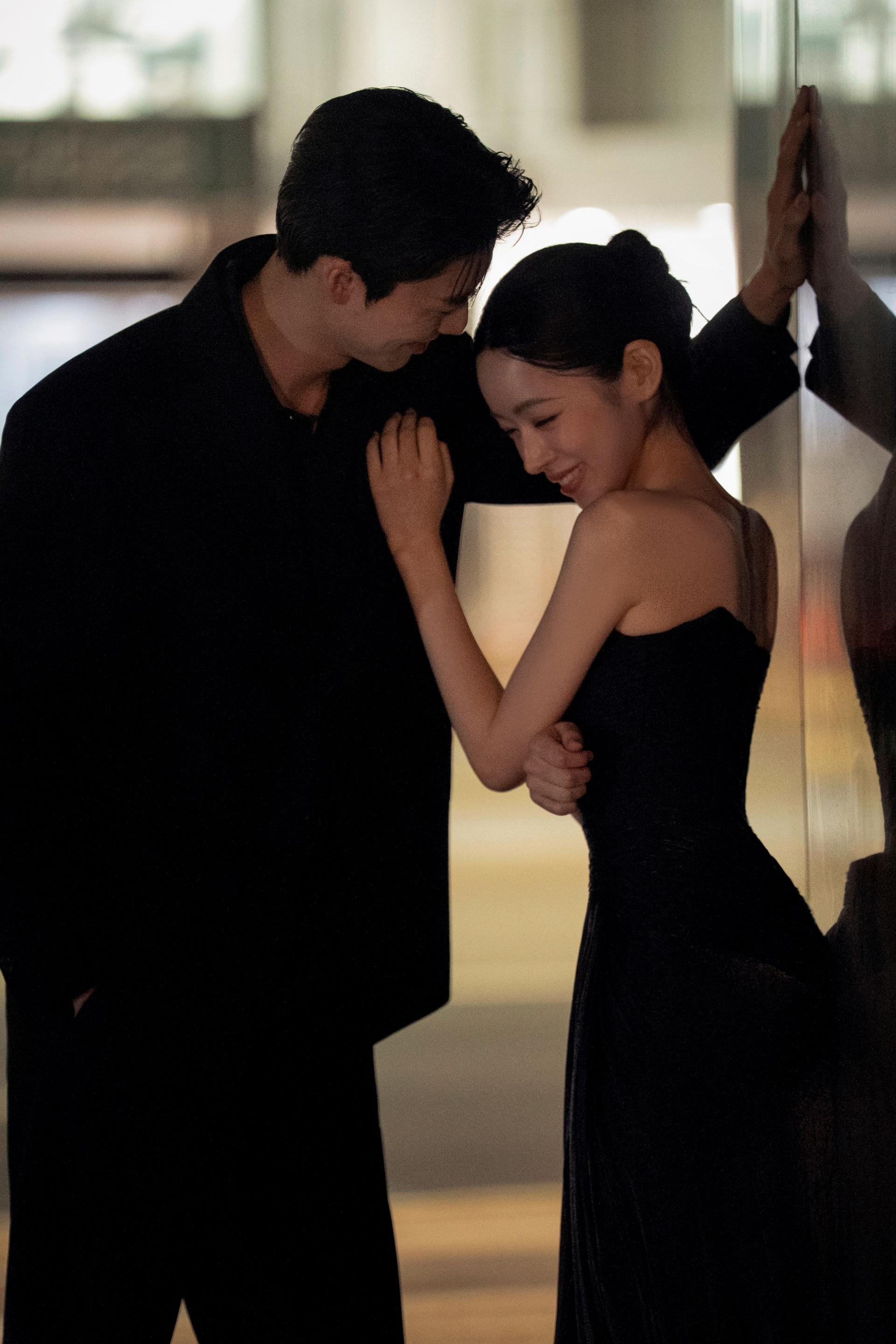 로렌하우스 웨딩 스튜디오 블랙 수트와 드레스를 입은 신랑 신부가 벽에 기대어 다정한 포즈를 취하고 있는 커플 웨딩 사진