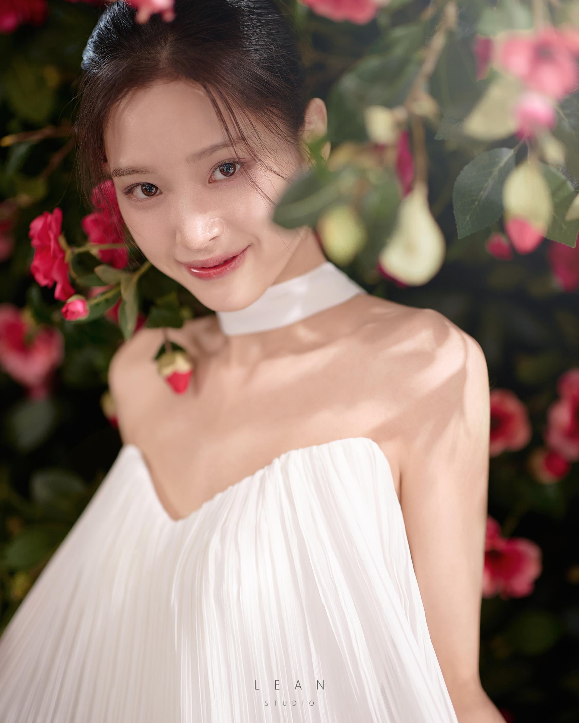르안스튜디오 웨딩 스튜디오 붉은 꽃과 짙은 녹음 사이에서 플리츠 웨딩드레스를 입은 신부의 얼굴과 표정을 담은 플라워씬 클로즈업 웨딩 촬영컷