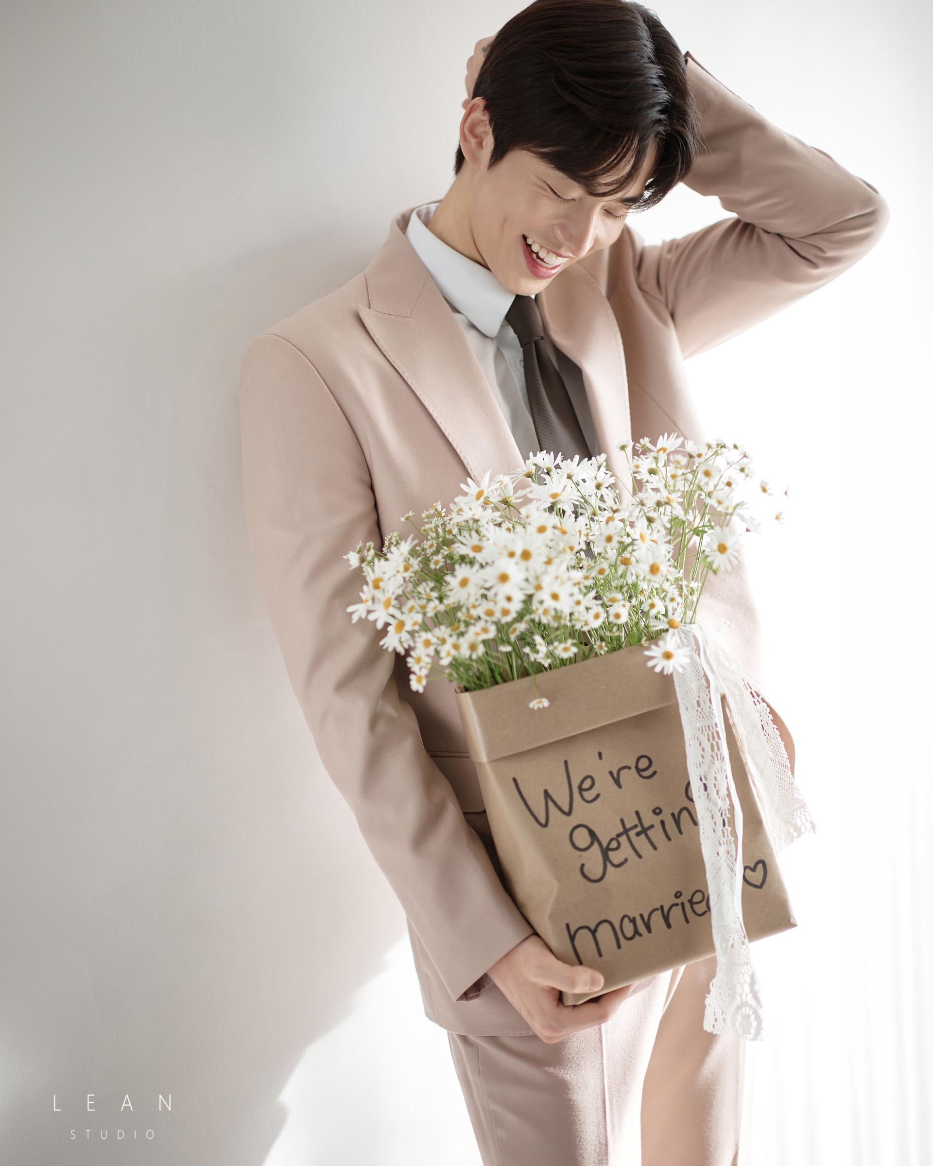 르안스튜디오 웨딩 스튜디오 화이트 데이지 꽃다발을 품에 안고 베이지 수트를 착용한 신랑이 자연스럽게 웃는 화사한 플라워 콘셉트 웨딩 촬영컷