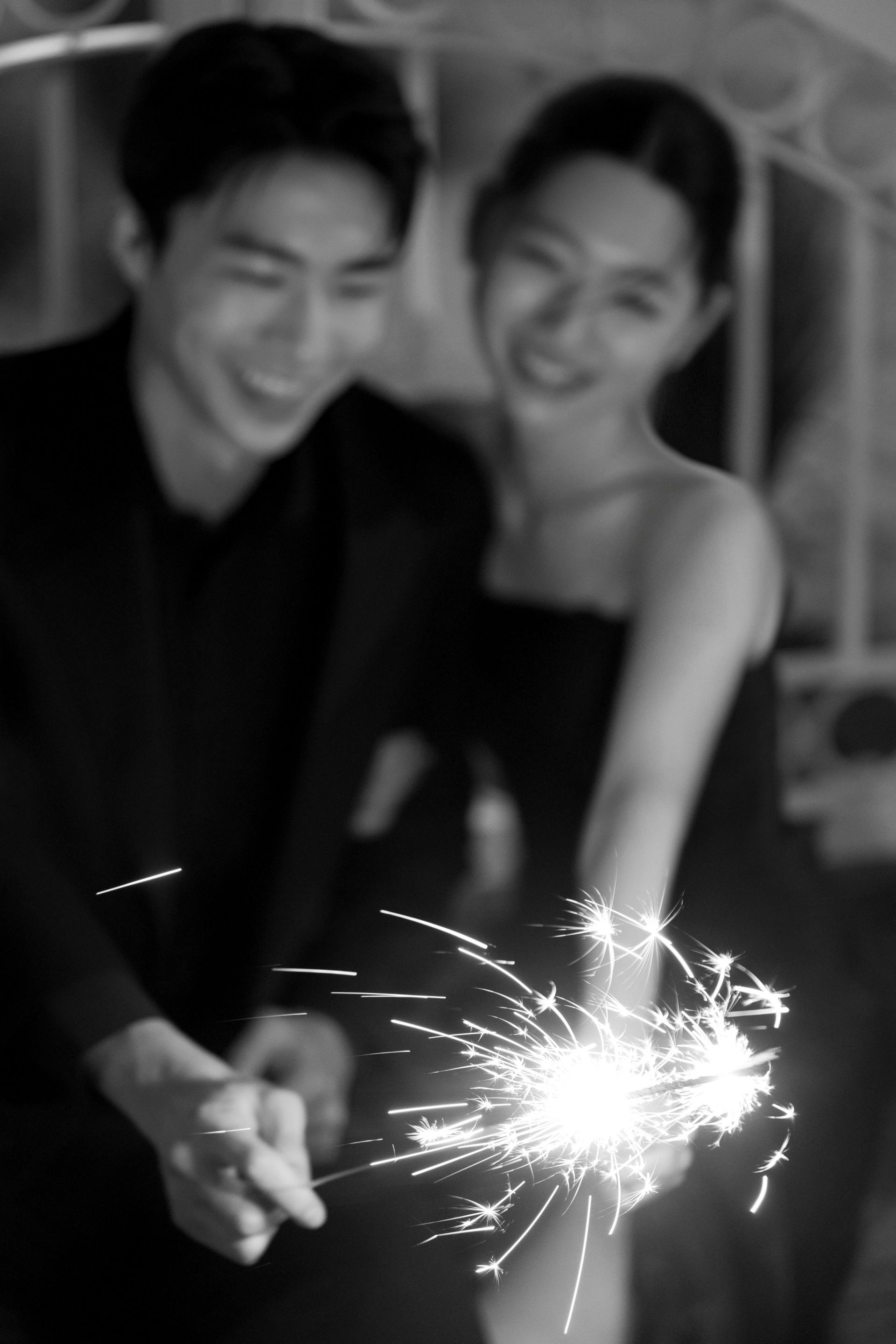 로렌하우스 웨딩 스튜디오 수트와 드레스를 입은 신랑 신부가 불꽃놀이 스틱을 들고 환하게 웃고 있는 모습을 흑백 감성으로 담은 커플 웨딩 사진