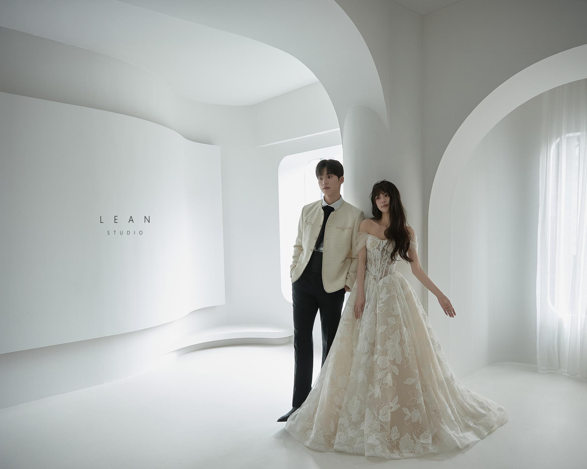 르안 스튜디오 웨딩 스튜디오 플라워 자수 디테일의 오프숄더 웨딩드레스를 입은 신부가 아이보리 재킷을 입은 신랑 곁에서 환하게 웃는 자연스러운 커플 클로즈업 웨딩 촬영컷
