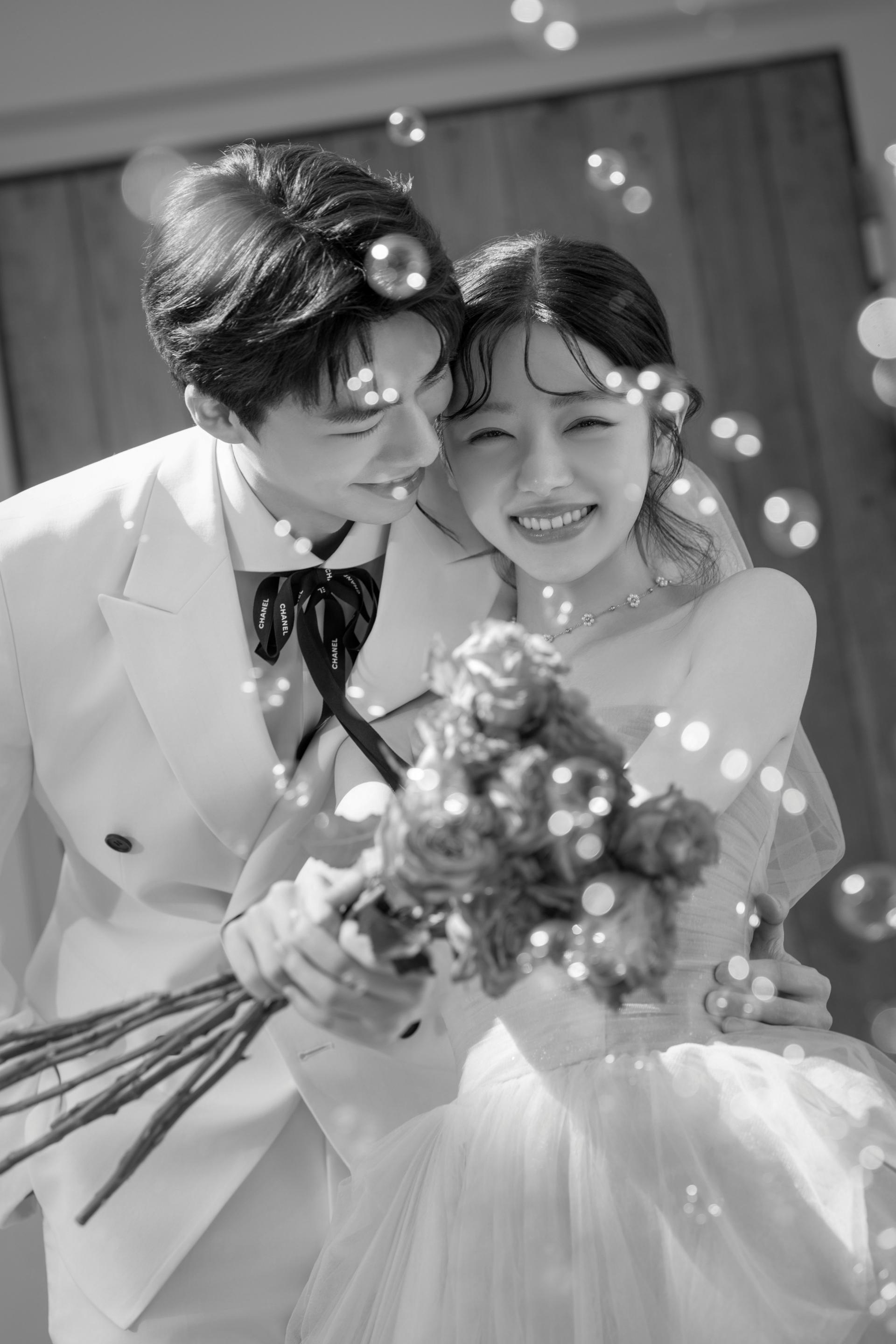로렌하우스 웨딩 스튜디오 화이트 수트를 입은 신랑과 드레스를 입은 신부가 부케를 함께 들고 비눗방울 속에서 환하게 웃고 있는 모습을 흑백 감성으로 담은 커플 웨딩 사진