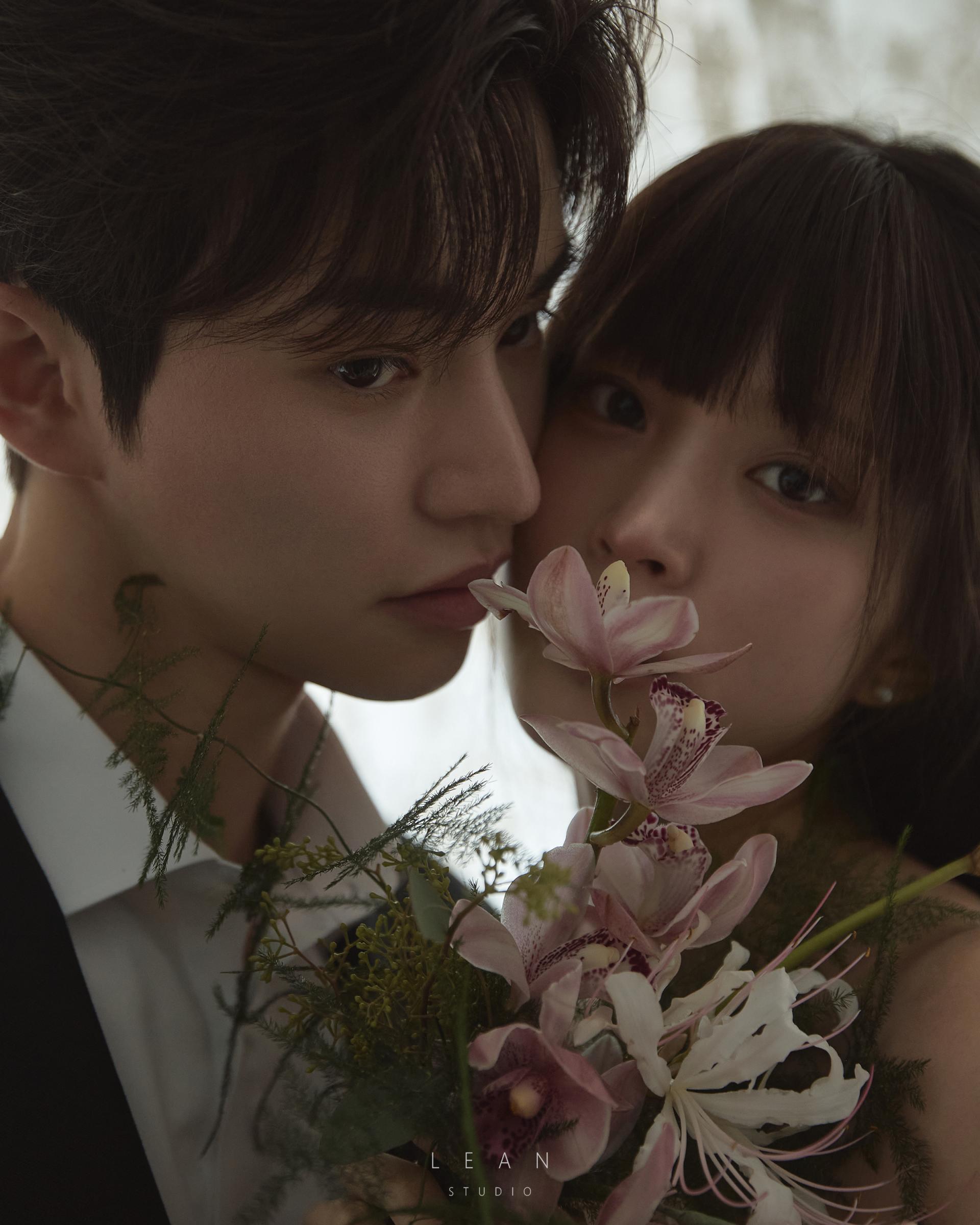 르안스튜디오 웨딩 스튜디오 핑크 오키드 플라워 부케를 사이에 두고 얼굴을 가까이 맞댄 신랑 신부의 무드 있는 클로즈업 웨딩 촬영컷