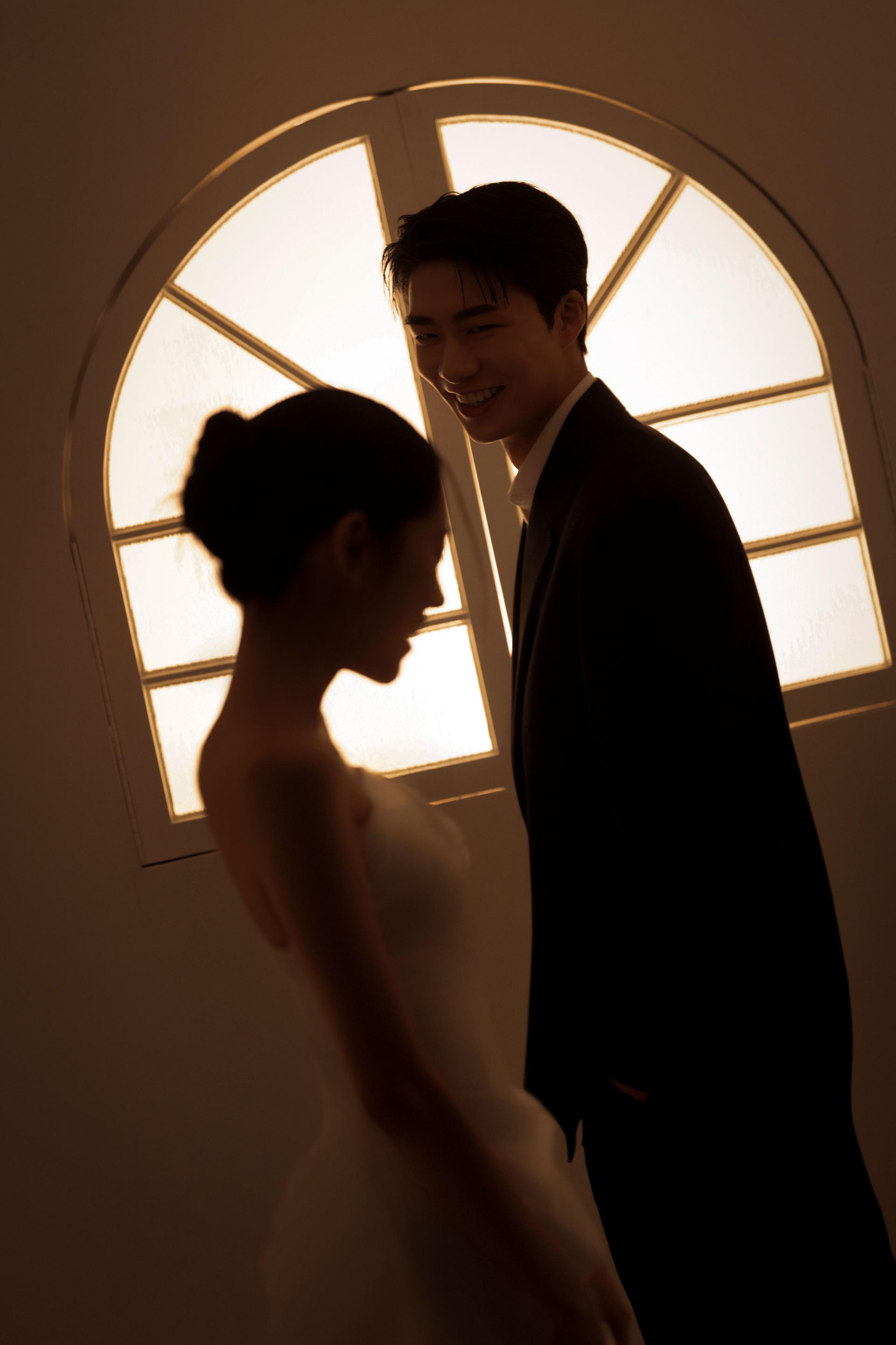 로렌하우스 웨딩 스튜디오 아치형 창문에서 새어 나오는 따뜻한 역광을 배경으로 신랑의 미소와 실루엣을 강조한 커플 웨딩 사진