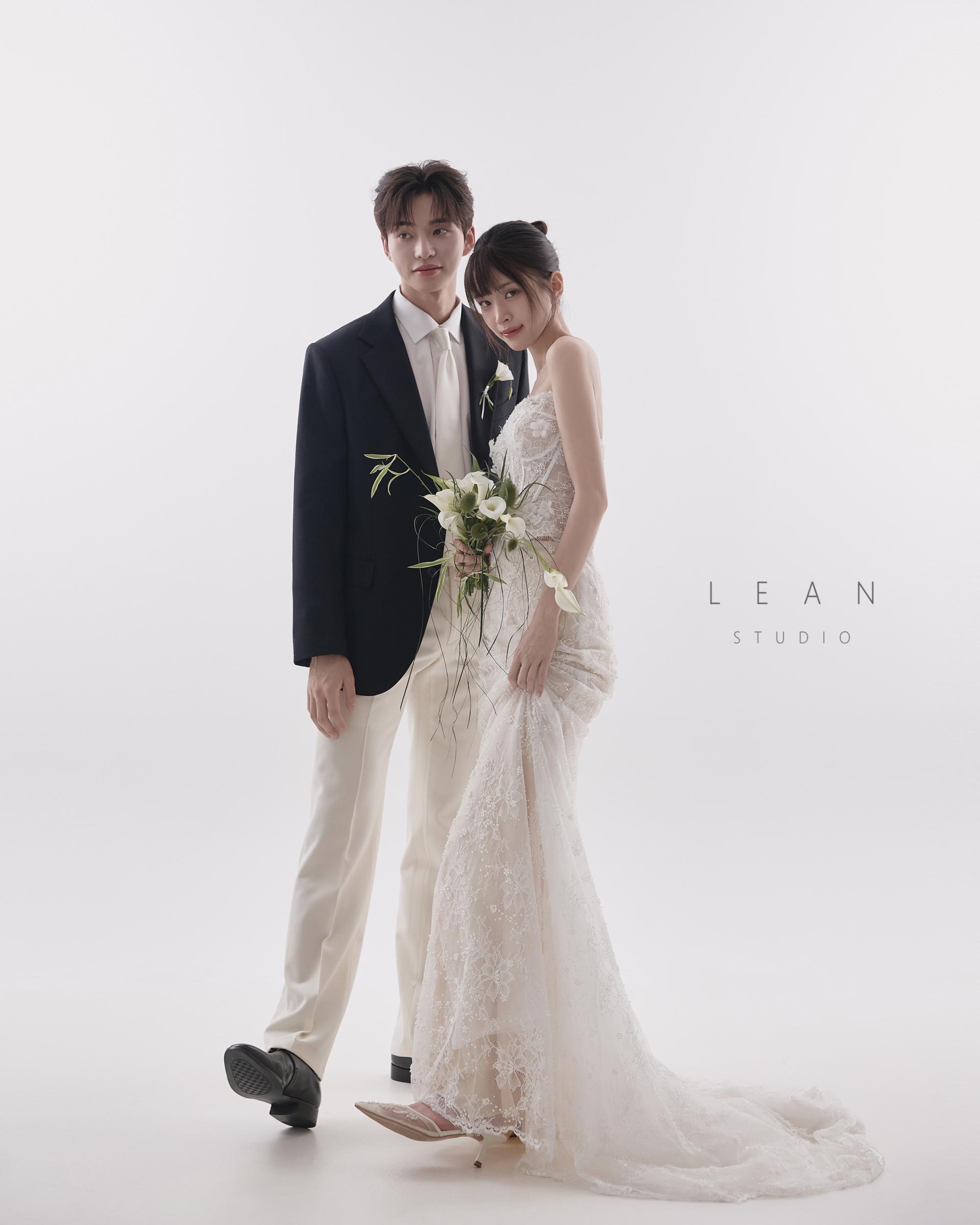 르안스튜디오 웨딩 스튜디오 화이트 배경에서 블랙 재킷과 아이보리 팬츠를 입은 신랑과 슬림한 레이스 웨딩드레스를 입은 신부가 나란히 선 전신 웨딩 촬영컷